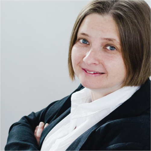 Blue-eyed, fair-skinned woman looking over her shoulder with arms crossed.